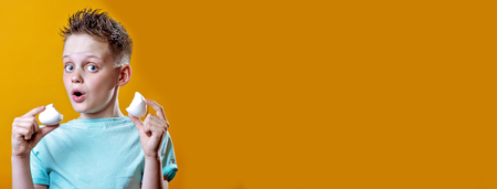 cheerful boy in a light t-shirt holding a broken egg on a bright colored backgroundの写真素材
