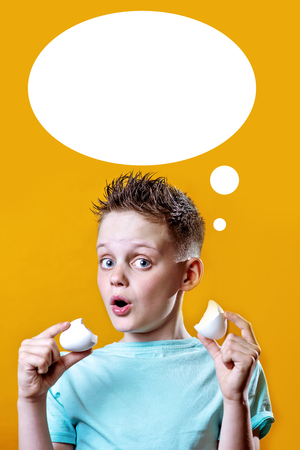 cheerful boy in a light t-shirt holding a broken egg on a bright colored backgroundの写真素材