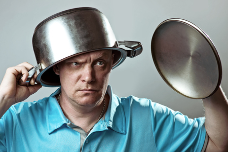 a bald brutal man in a blue t-shirt put a pot on his headの写真素材