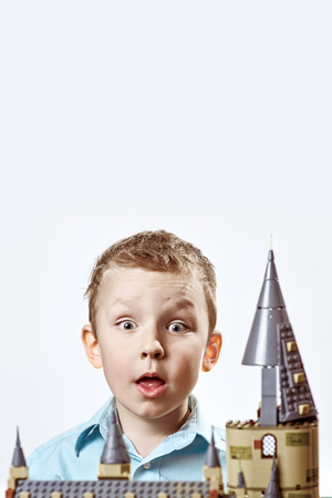 the surprised boy in a light shirt looks out from the constructed lock of the designer on a light backgroundの写真素材