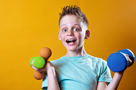 a boy in a blue t-shirt with dumbbells on a bright yellow backgroundの写真素材