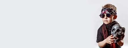 boy rocker in black glasses, scarf, bandana and with a skull in his hands on a light backgroundの写真素材