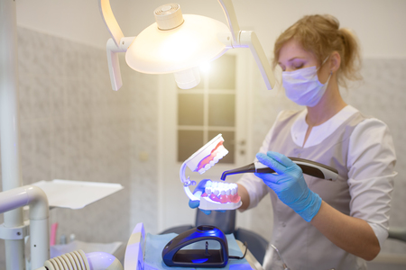 the doctor shows the jaw how to use a modern photo polymerization lamp in the dental officeの写真素材