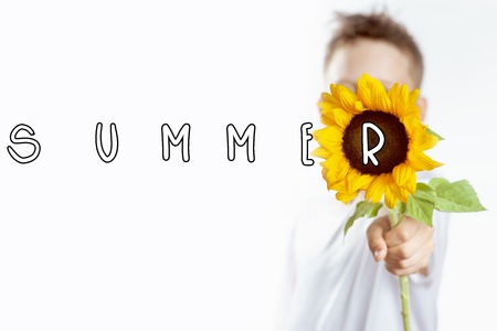 summer boy in a light t-shirt with a yellow sunflower covers his faceの写真素材