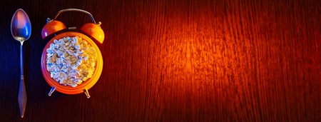 Concept on the topic of Wake up it's morning. Oatmeal in an orange alarm clock, and next to the spoon.の写真素材