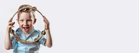 a cheerful boy in a blue shirt holding a tambourine and smiling on a light backgroundの写真素材