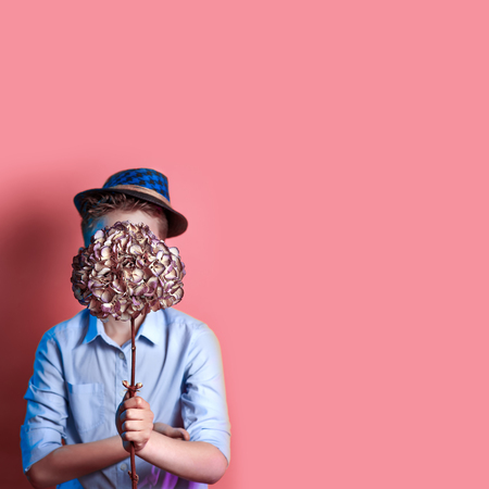 a man in a hat holding a bouquet in front of his face on a bright colored backgroundの写真素材