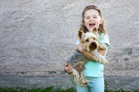 cute girl in a blue t-shirt with dimples on her cheeks holding a dog and smilingの写真素材
