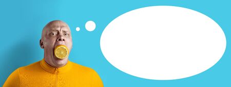 bald brutal man with lemon in his mouth and yellow jacket on a blue backgroundの写真素材