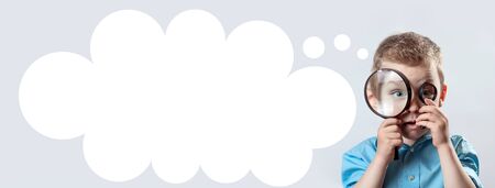 a boy in a light t-shirt looking into a large magnifying glassの写真素材