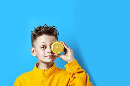 a boy in a bright yellow jacket with a lemon in his hand on a blue backgroundの写真素材