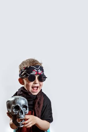 boy rocker in black glasses, scarf, bandana and with a skull in his hands on a light backgroundの写真素材