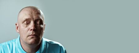 a bald brutal man in a light t-shirt put matches in his eyes and sleepsの写真素材