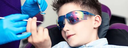 the boy in special glasses in the dentist's chair. he curiously studies medical instruments in the hands of a doctor.の写真素材