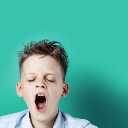 the boy in the blue t-shirt is tired, wants to sleep and yawns