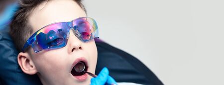 The boy with goggles in the dental chair. The doctor examines the oral cavity with a special dental mirrorの写真素材
