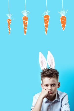 bored boy in a light shirt and Bunny ears on a blue backgroundの写真素材