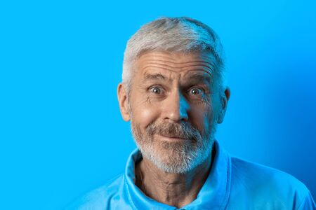 portrait of a surprised and curious gray-haired man with a beard on a blue background