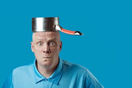 a bald brutal man in a blue t-shirt put a pot on his headの写真素材