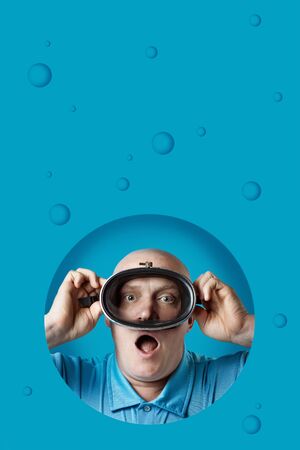 bald brutal man in a diving mask holds his breath on blue backgroundの写真素材
