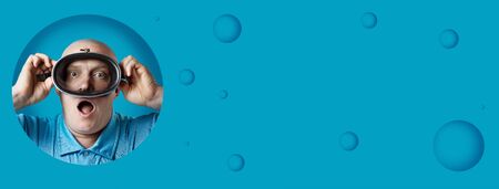 bald brutal man in a diving mask holds his breath on a blue backgroundの写真素材