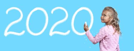 Cute girl with white chalk on blue background. Writes on the Board 2020 yearの写真素材