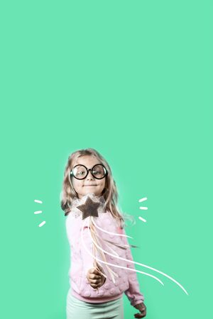 girl with glasses and a magic wand says a spell on a green backgroundの写真素材