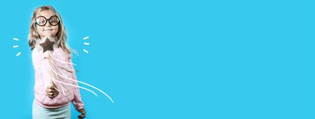 girl with glasses and a magic wand says a spell on a blue backgroundの写真素材