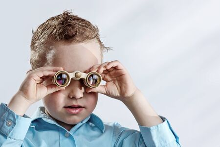 a boy in a light shirt looking through binoculars on a light backgroundの写真素材