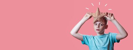 a boy in a light t-shirt holding a starfish on a bright pink background