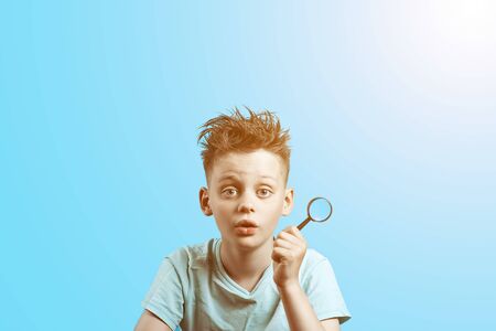 a boy in a light t-shirt holding a small magnifying glass on blue backgroundの写真素材