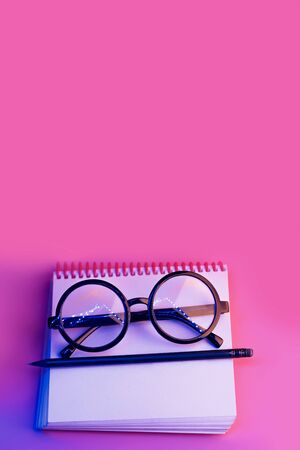 black round glasses lie on a Notepad in neon light on a pink backgroundの写真素材