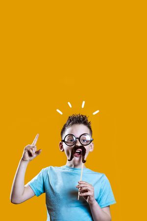 a boy in a light t-shirt with a mustache and glasses holds his index finger up against a bright backgroundの写真素材