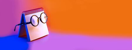 black round glasses lie on a Notepad in neon light on a pink backgroundの写真素材