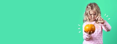 cute witch girl with blonde hair conjures over a pumpkin on a colored backgroundの写真素材