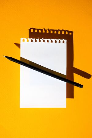 a blank sheet of Notepad, black pencil and hard shadows on bright yellow backgroundの写真素材