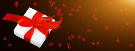 White gift box with a red ribbon and a scattering of stars on a black background.の写真素材