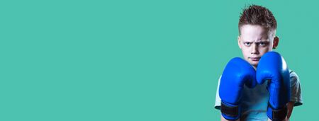 Severe boy in blue Boxing gloves on bright mint backgroundの写真素材