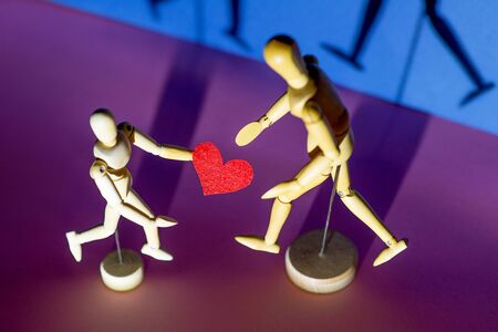 Two wooden men hold their hearts in their hands. On a blue background.の写真素材