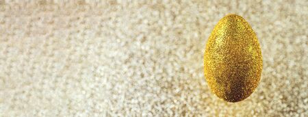 A golden egg hangs in the air. On a textured gold background. The concept on the theme of Easter.の写真素材