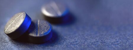 Three black activated charcoal tablets. On a black background. There's blue light on the side. Bannerの写真素材