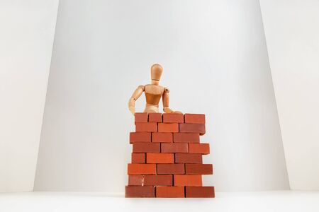 A wooden man builds a brick wall around him. Concept on self-isolation and coronavirus.の写真素材