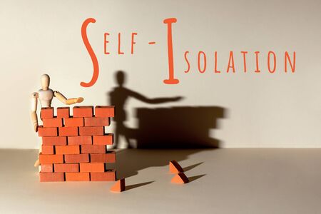 A wooden man builds a brick wall around him. Concept on self-isolation and coronavirus.の写真素材