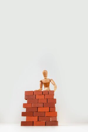 A wooden man builds a brick wall around him. Concept on self-isolation and coronavirus.の写真素材