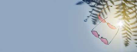 Pink heart glasses with palm tree shadows on a blue background.