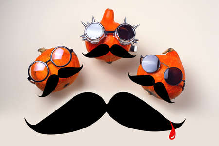 Three orange rocker pumpkins with glasses and a mustache on a light background. Halloween concept.