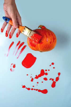 The hand with the brush paints the pumpkin red. Paint is like blood. Nearby spots, drops, sprays, stains, splashes. Halloween concept.の写真素材