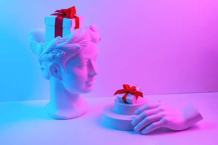 Composition with gypsum bust and hand. A box with a red ribbon in head and on the podium. Gift concept.の写真素材