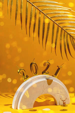 Golden candles with the new year 2021 on the marble arch, palm leaves, column, stairs, balls, Christmas trees, confetti on a yellow background with the horizon. Festive trend still life.の写真素材