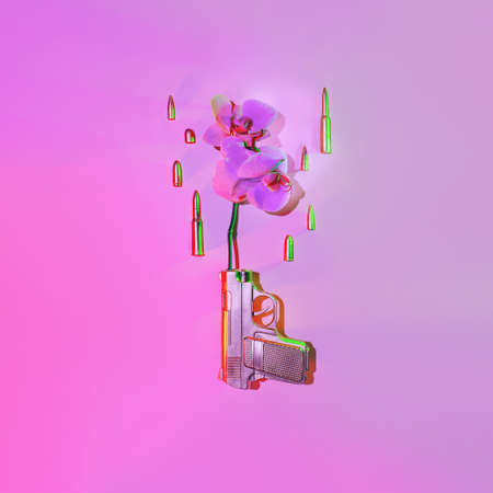 The golden gun shoots an orchid flower, next to fly bullets on a pink background, the concept...
